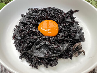 Black squid ink risotto with squid and yolk egg on top.