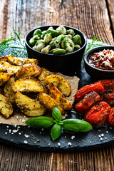 Boiled broad bean with roasted potatoes and cherry tomatoes with tomato pesto on wooden table