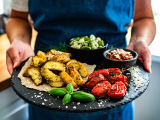 Woman holding stone board with boiled broad bean with roasted potatoes and cherry tomatoes with...