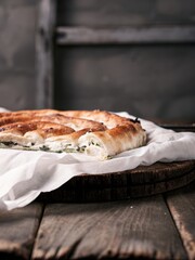 Flaky pastry layers of Serbian burek pastry with melted cheese filling and herbs on a wooden table