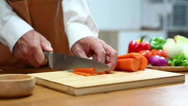 Closeup of hands slicing fresh carrot on a wooden board in clean kitchen. Healthy cooking, diet food prep, organic vegetables,