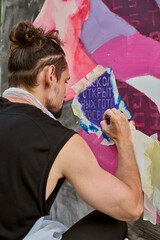 Young male artist with styled hair paints vibrant portrait outdoors. Detailed brushwork on colorful...