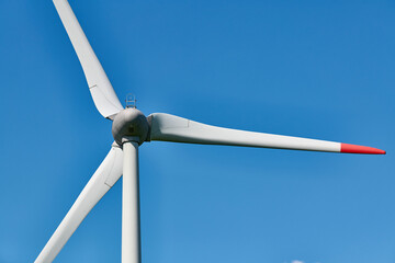 Detailed view of wind turbine with red tipped blades set against clear, vibrant blue sky on sunny...