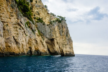 Towering limestone cliffs and dramatic Keri sea caves in Zakynthos, Greece, captured from the water under a soft cloudy Ionian sky.

