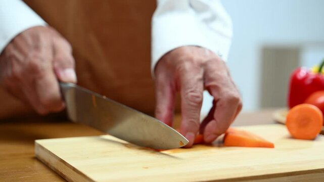 Closeup of hands slicing fresh carrot on a wooden board in clean kitchen. Healthy cooking, diet food prep, organic vegetables,