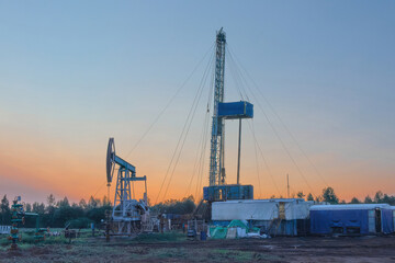 Obraz premium Drilling a well in an oil field. In the foreground is a mobile drilling rig. In the background, oil production at the field using a rocking machine. Summer. Beautiful sky and nature.