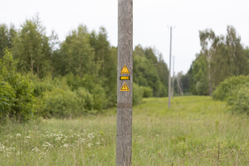 Wooden Utility Pole with Warning Signs in a Rural Green Landscape