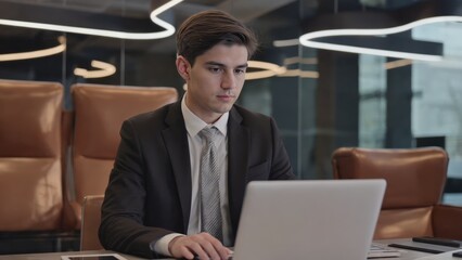 Fototapeta premium A man in a suit sitting at a desk with his laptop, focused on work.