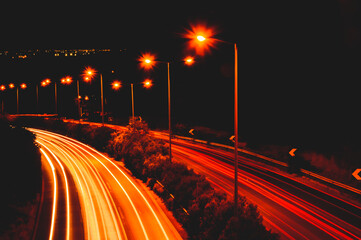 Long exposure of highway at night with car light trails and street lamps glowing orange, creating a...