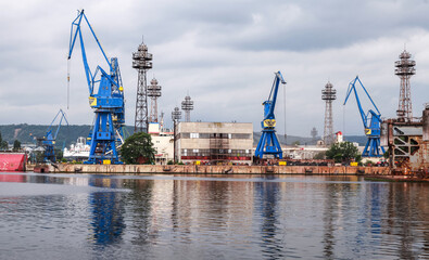Industrial dockyard showcasing large blue cranes, buildings, and docked ships