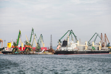 Obraz premium Cargo ships docked at an industrial port, surrounded by numerous cranes