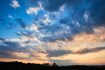 Breathtaking sky filled with dramatic clouds transitions from deep blue to soft pastels as sun...