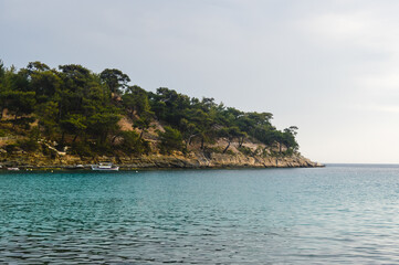 Obraz premium Rocky coastline and turquoise waters in Aliki, Thassos island, Greece, with pine trees and traditional fishing boat under soft summer light.