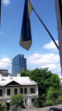 Ukrainian flag waving against blue sky. Cityscape view