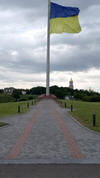 Ukraine flag waves on flagpole. Gray stone road on foreground
