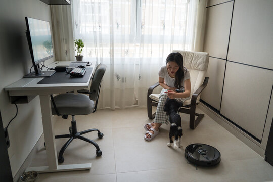 Home office with asian woman, dog, and robot cleaner