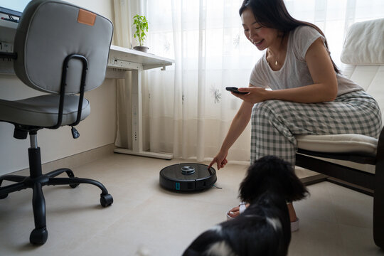 Asian woman with dog and robot vacuum at home office