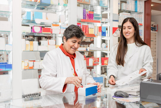 Two female pharmacists working together in a pharmacy checking medicine and a prescription