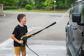Child cleaning car with a pressure washer outdoors