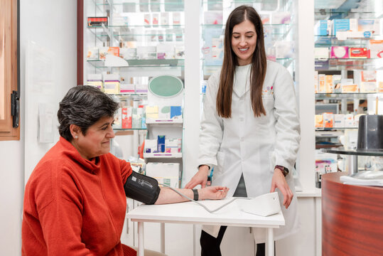 Smiling female pharmacist measuring blood pressure of senior woman customer in a pharmacy