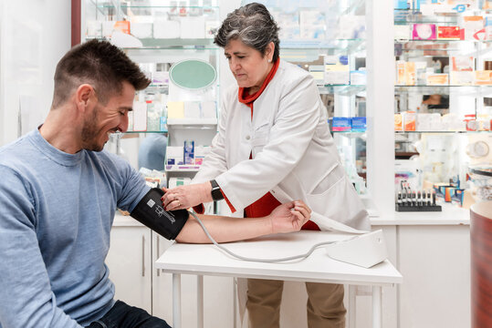 Senior woman Pharmacist measuring blood pressure of male customer in pharmacy - Powered by Adobe