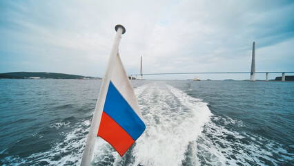 Sailing boat traversing waters near russky bridge, russian flag fluttering against cloudy skyline, capturing maritime panorama in vladivostok