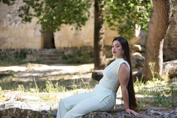 Young, beautiful, brunette woman in a white dress, relaxed and calm looking at camera sitting on a...
