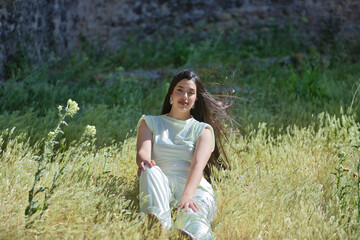 Young, pretty, brunette woman in a white dress, looking at camera, relaxed and calm, sitting among...