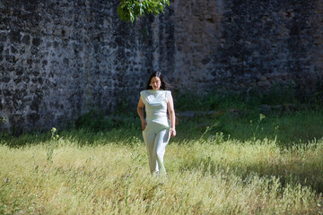 Young, pretty, brunette woman in a white dress, relaxed and calm, walking in the tall grass on a...
