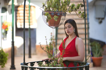 Young, pretty, brunette woman in a nice red party dress, posing relaxed and calmly leaning on a...