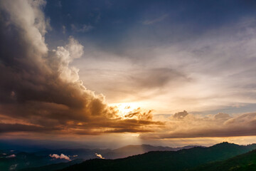 dramatic sunset over majestic mountains as golden sun rays pierce through a cloudy sky before rain, casting light over the vast scenic landscape below