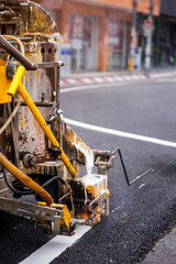 A close-up of a road marking machine in action, precisely painting a crisp white line on fresh asphalt. This highlights essential road maintenance.
