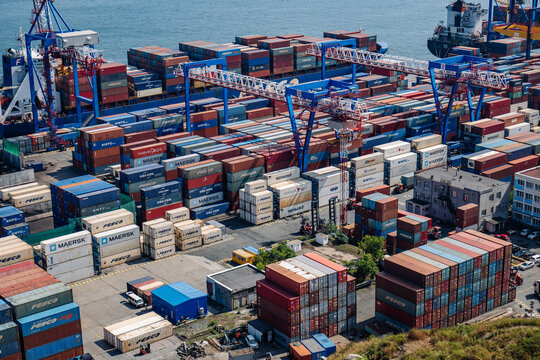 Vladivostok, Russia - August 9, 2021: Cargo cranes loading colorful containers in the port of vladivostok, russia, with the zolotoy rog bridge in the background