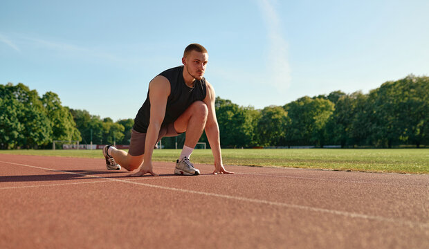 Focused male runner at starting position on track at sunrise