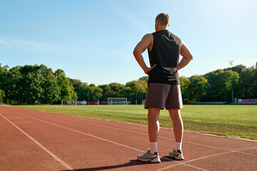 Fit man standing on stadium track looking ahead with hands on hips