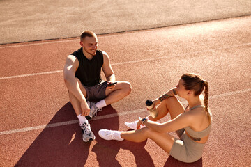 Fit couple resting after workout and talking on running track