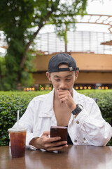 Non binary gay man drinking iced coffee in outdoors cafe restaurant and using mobile phone