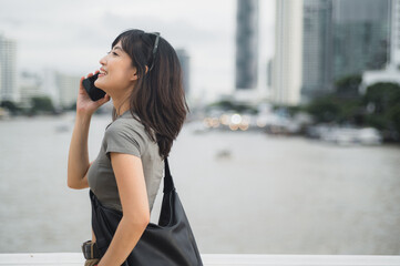 Happy solo Southeast Asian woman teenager travel blogger uses smartphone. An explorer enjoying...