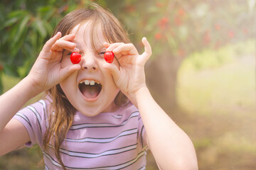 Child plays with cherries while smiling outdoors under a sunny sky