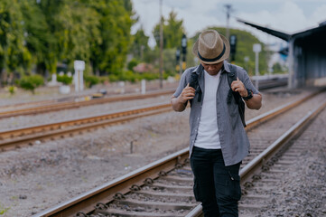 Asian man traveler with backpack in the railway. Traveler man wearing hat walking on the train...