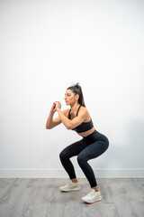 Woman performing a squat with proper form on wooden floor in minimalistic white room