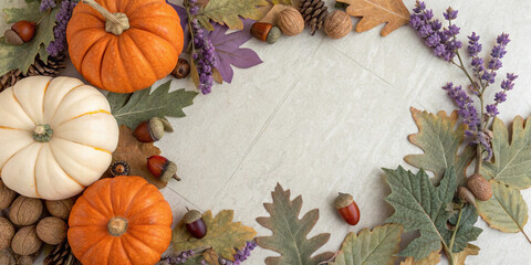Colorful pumpkins, acorns, dry leaves, walnuts, pine cones, and lavender flowers are creating a beautiful autumnal frame on a textured surface, perfect for thanksgiving or halloween projects