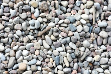Close-up view of small pebbles creating a natural pattern and texture. Tiny gravel stones in various earthy tones form a seamless background, ideal for use in design or nature-themed projects.