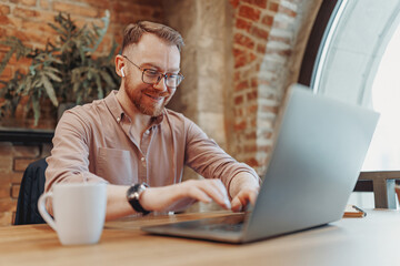 A smiling man focused on his laptop in a modern caf with warm decor