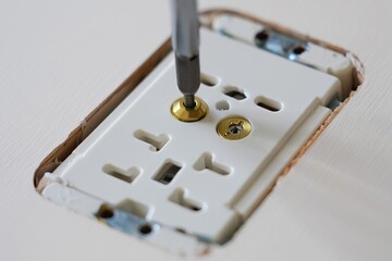Electrical outlet installation process featuring a screwdriver tightening screws on a white wall plate, showcasing the intricate details of home improvement and electrical work