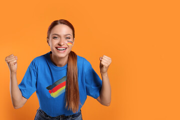 Excited fan with flags of Germany on her cheek and t-shirt against orange background. Space for text