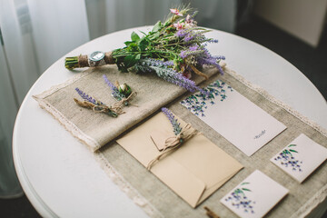 Rustic lavender-themed wedding stationery and bouquet on linen tablecloth, symbolizing romance, craftsmanship, slow lifestyle, authenticity, and attention to natural details.
