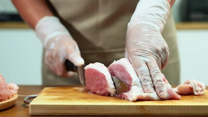 Closeup of a gloved hand slicing raw pork loin on a wooden board in a clean kitchen. Perfect for culinary, food prep