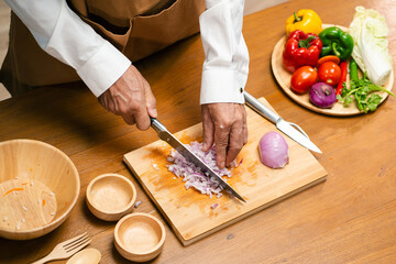 Close up of Asian man's hands cutting onions on a wooden cutting board in a kitchen, preparation...