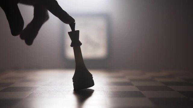 The man hand gently wiggles chess piece on the chessboard with his index finger